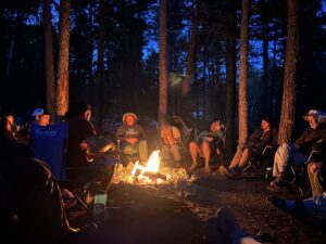 10 people sitting around a large campfire at night after a day of trail work