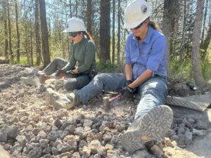 Two volunteers sit on the ground while making crush at Yellowstone National Park. 