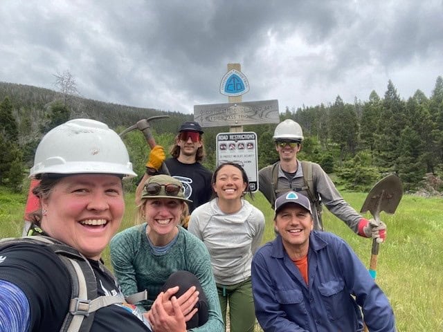 Employees of team OBOZ smiling with trail tools in front of a CDT sign.