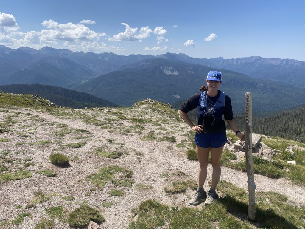 1 person on a trail next to a sign post overlooking lots of mountains