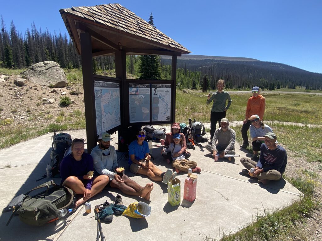 A group of hikers sitting and standing at kiosk enjoying some cold drinks