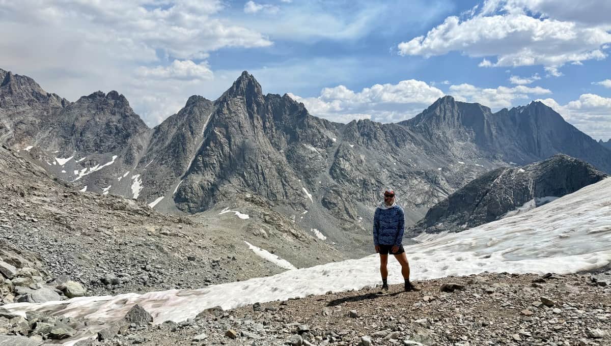 Hiker standing at a high alpine pass in the Wind River Range with jagged granite peaks and glacial snow in the background